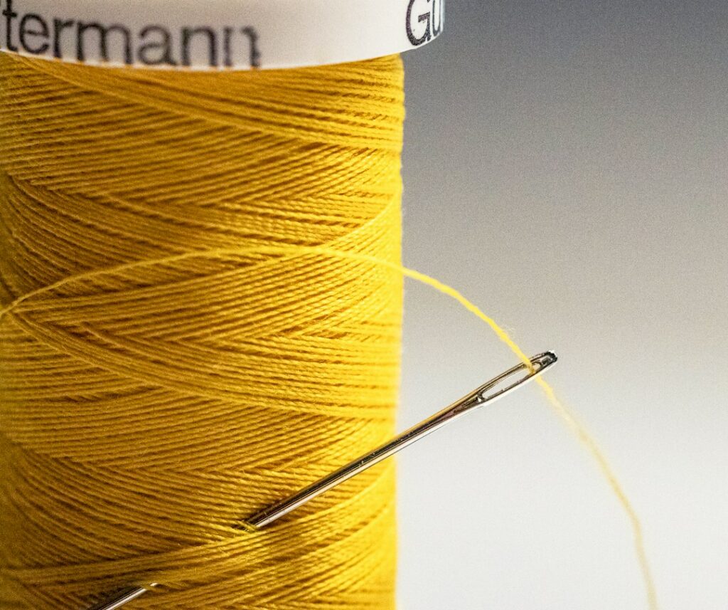 Aiguille à coudre enfilée, piquée dans une bobine de fil jaune